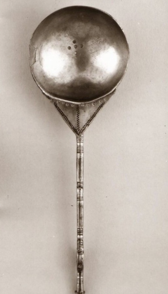 A gilt silver spoon consisting of a hemispherical bowl with five holes punched in the centre, joined to a triangular plate, which connects to a thin stem.